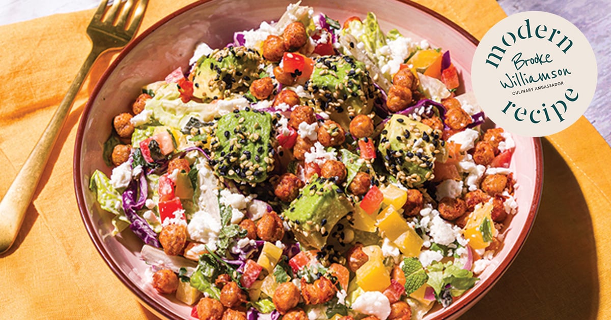Bowl of chickpea and avocado salad with mixed greens, diced vegetables, feta, and sesame seeds, served on a table in bright natural light with a Modern Recipe label visible.