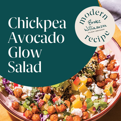 Bowl of chickpea and avocado salad with mixed greens, diced vegetables, feta, and sesame seeds, served on a table in bright natural light with a Modern Recipe label visible.