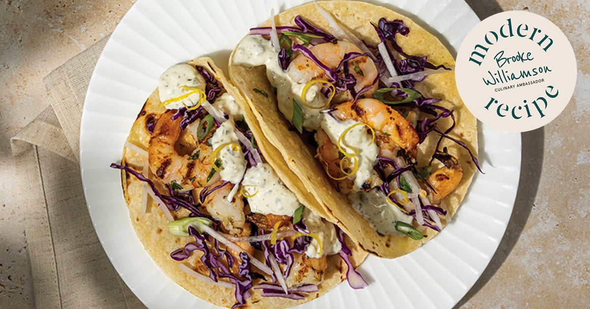 Overhead view of shrimp tacos topped with purple cabbage, herbs, and creamy sauce on a white plate, with a modern recipe badge in the corner indicating culinary inspiration.