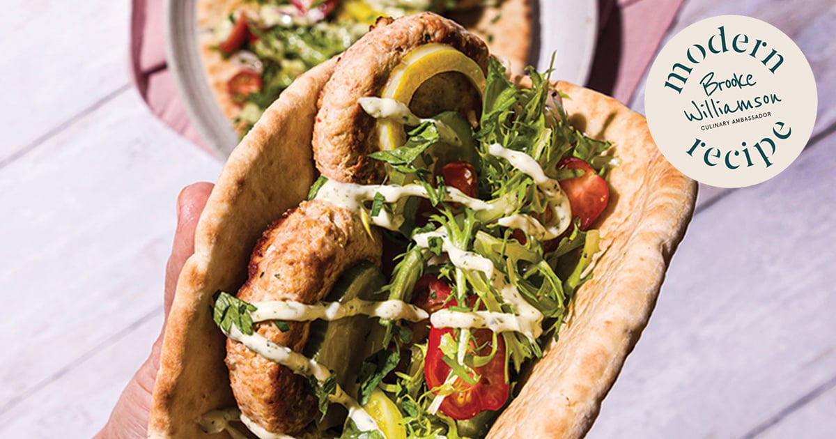 Hand holding a pita filled with kofta, fresh herbs, tomatoes, and sauce, photographed in bright natural light with a Modern Recipe label visible.