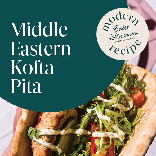Hand holding a pita filled with kofta, fresh herbs, tomatoes, and sauce, photographed in bright natural light with a Modern Recipe label visible.