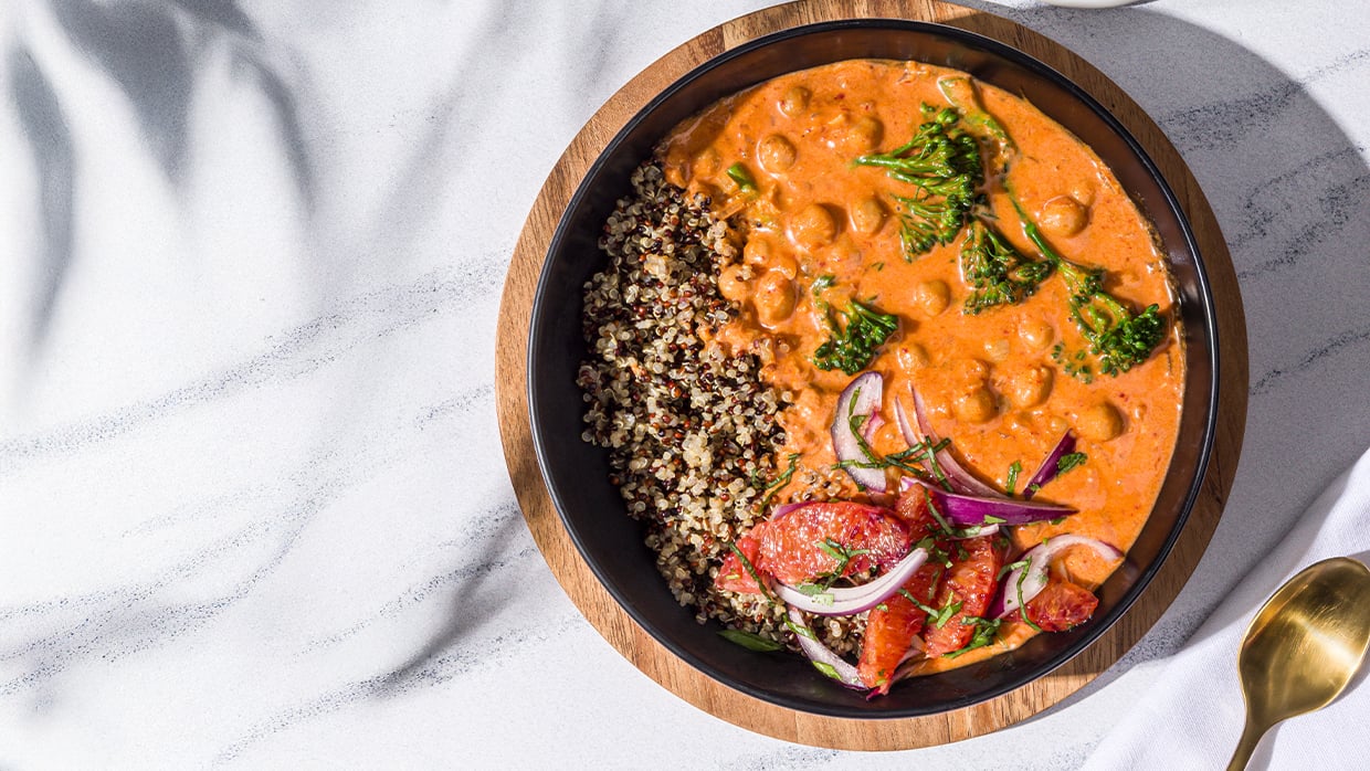 Bowl of quinoa, chickpea curry, broccoli, and roasted veggies on marble surface with a gold spoon.