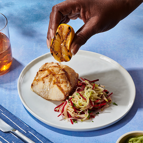 Hand of a black person squeezing a lemon over a salmon with vegetables