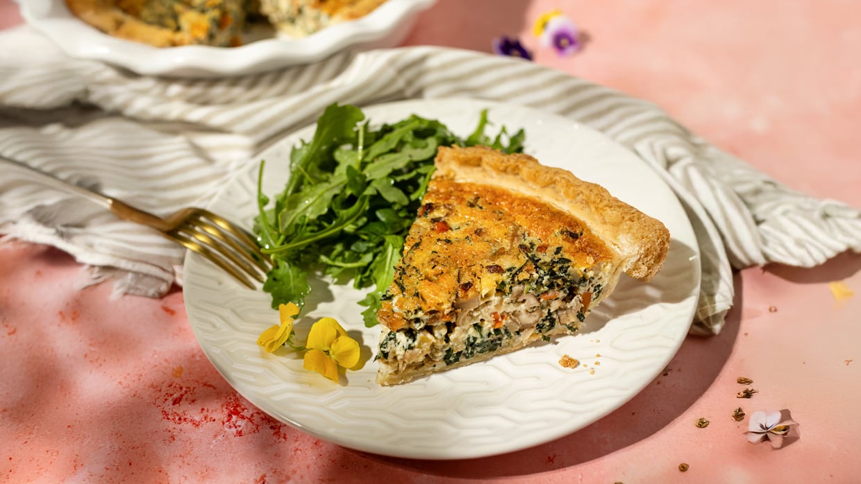 slice of quiche with spinach and arugula salad on a white plate