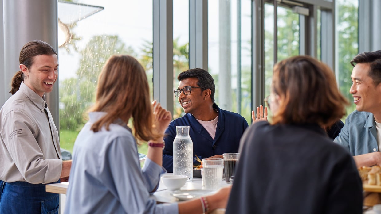 three people talking and smiling around a table near a window