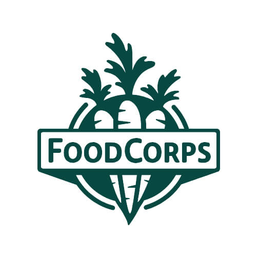 Logo for FoodCorps featuring three stylized carrots with leafy tops arranged in a circular pattern, with the name 'FoodCorps' prominently displayed in a green monochromatic color scheme, symbolizing their mission to connect kids to healthy food in schools.