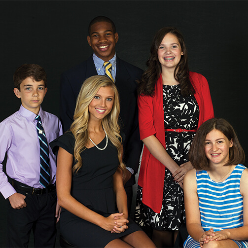 Group photo of five individuals: three adults in formal attire and two children dressed semi-formally, posed against a plain dark backdrop.
