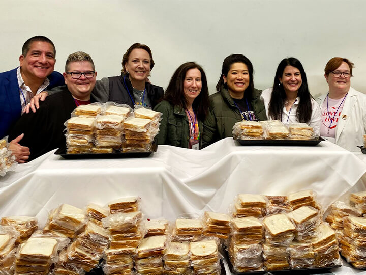 A group of five people smiling and posing together, each holding a sandwich in their hands.