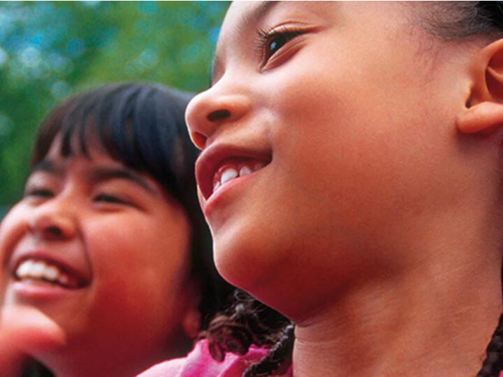 The image shows a close-up of two children, set outdoors against a backdrop of greenery, symbolizing innocence and a natural environment.