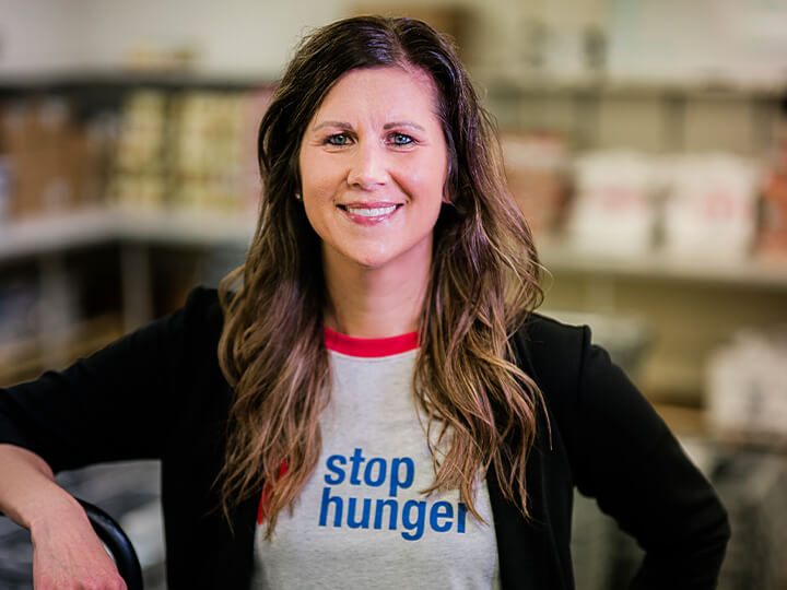 A woman wearing a t-shirt that reads "Stop Hunger" stands confidently, advocating for food security awareness.