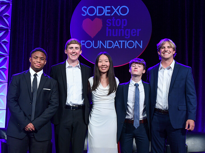 Group of five individuals standing in front of a 'SODEXO stop hunger FOUNDATION' backdrop, dressed in formal attire, suggesting an event related to hunger relief efforts.