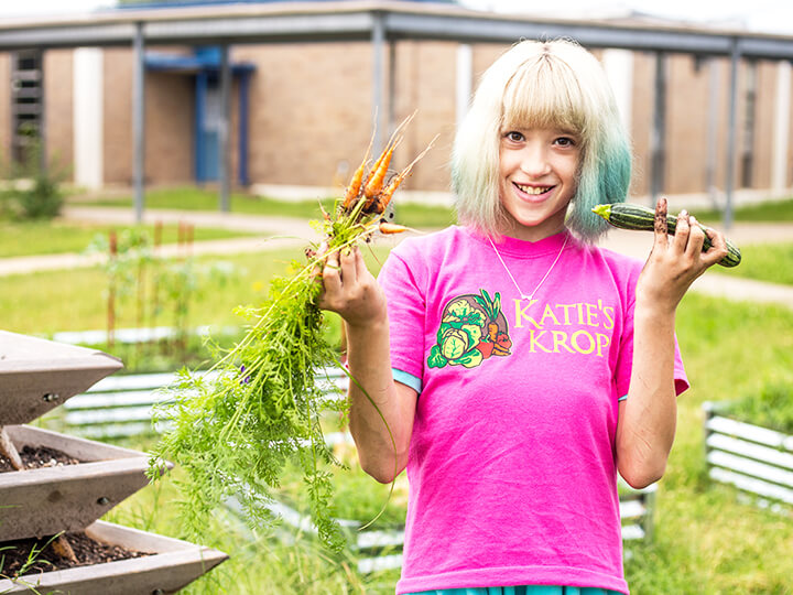 A girl smiling while holding a large orange carrot in her hands, showcasing her enjoyment of healthy food.
