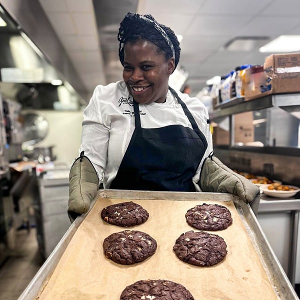 A woman presents a tray filled with freshly baked chocolate cookies, showcasing her culinary creation.