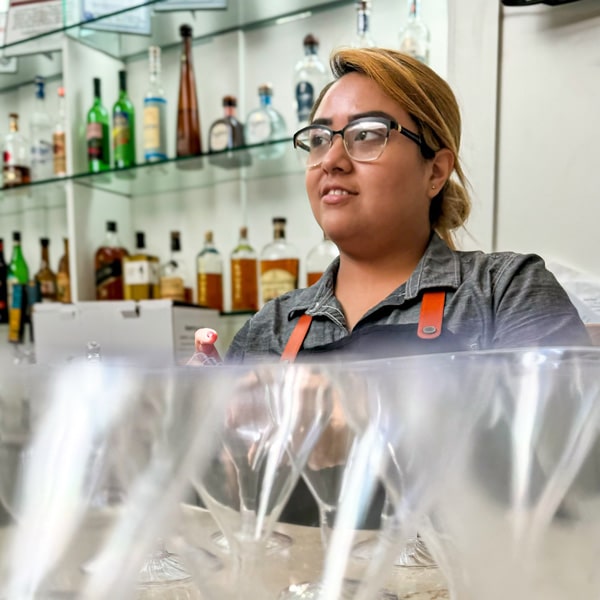 A woman wearing glasses skillfully prepares drinks at a bar, showcasing her expertise in mixology.