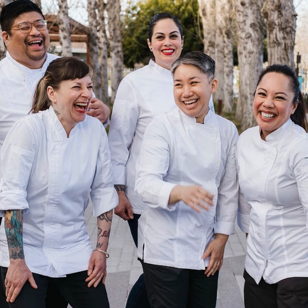 Chefs joyfully smiling and laughing together in a vibrant kitchen setting, showcasing camaraderie and teamwork.