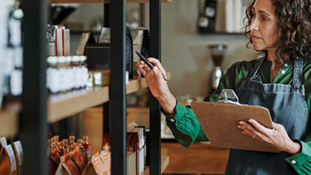 A woman in an apron examines a clipboard, focused on her task in a well-lit kitchen environment