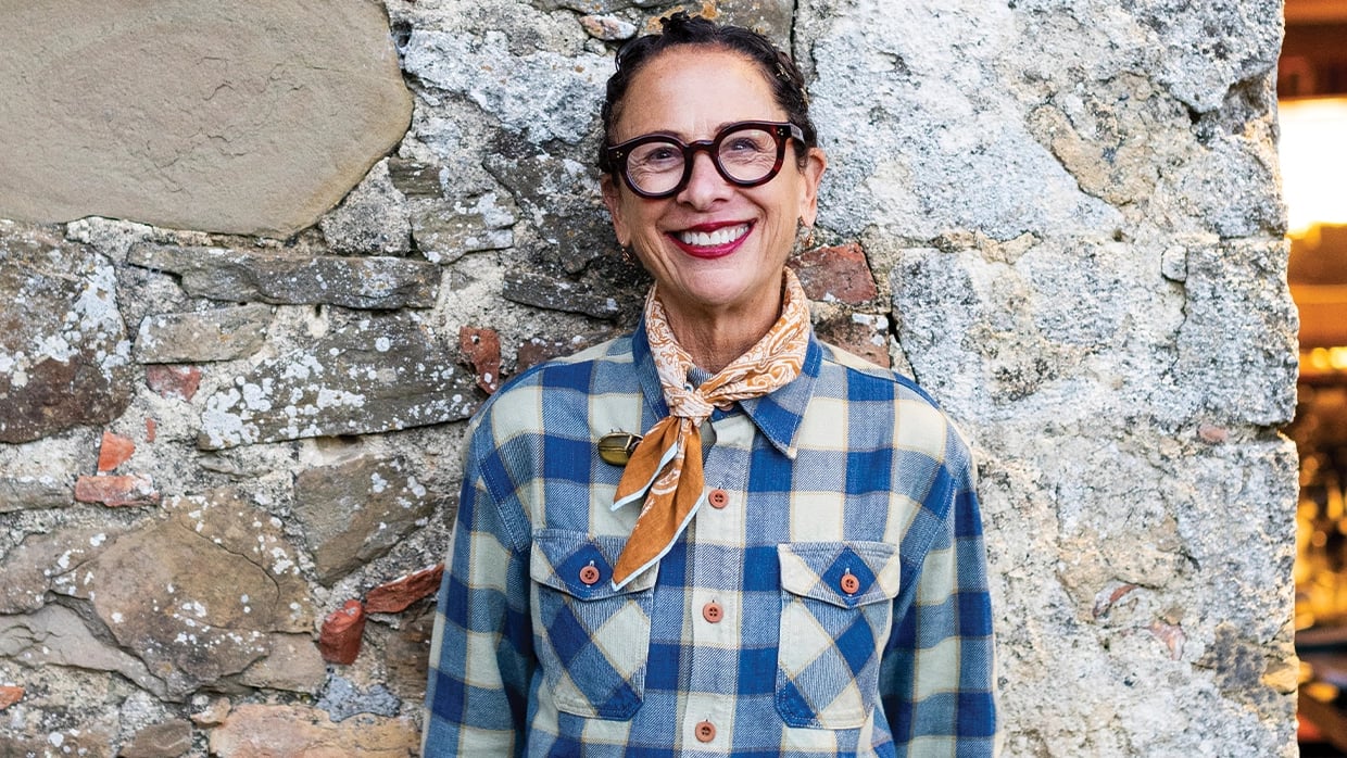 Person in glasses and plaid shirt smiling in front of a stone wall background.