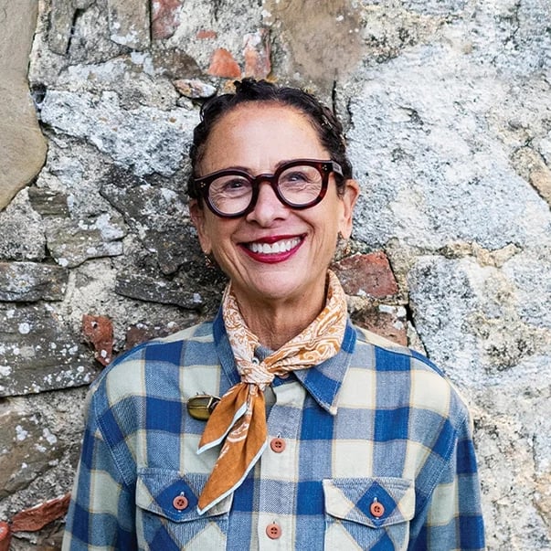 Person in glasses and plaid shirt smiling in front of a stone wall background.