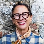 Person with glasses and scarf smiling in front of a stone wall.