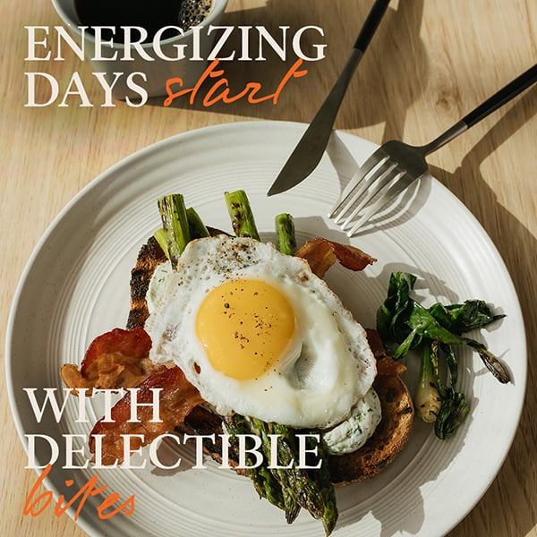 Plate with toast topped with asparagus, bacon, and sunny-side-up egg, leafy greens on the side. Text reads: 'ENERGIZING DAYS start WITH DELECTIBLE bites'.