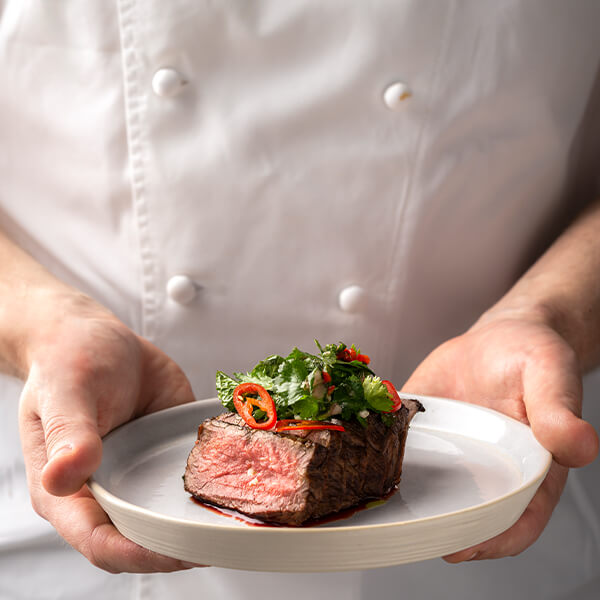 A chef proudly presents a plate featuring a beautifully cooked piece of meat, showcasing culinary expertise.