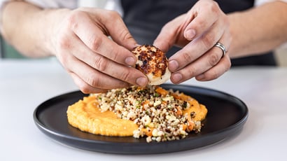 Hands plating a seared scallop with quinoa salad and creamy orange puree.