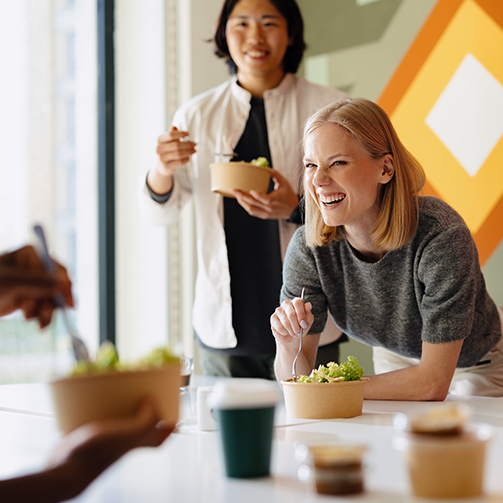 People eating salads at a table with vibrant geometric wall art in the background.