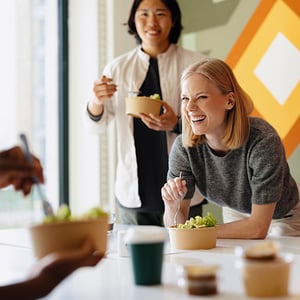 People eating salads at a table with vibrant geometric wall art in the background.