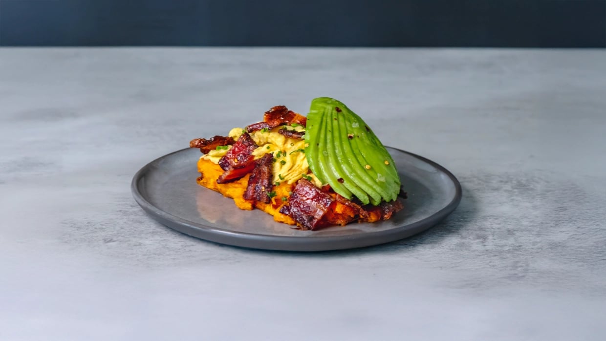 Sweet potato toast with scrambled eggs, bacon, and avocado on a plate.