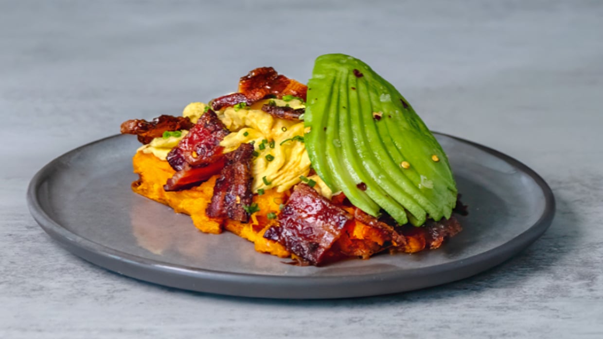 Sweet potato toast with scrambled eggs, bacon, and avocado on a plate.