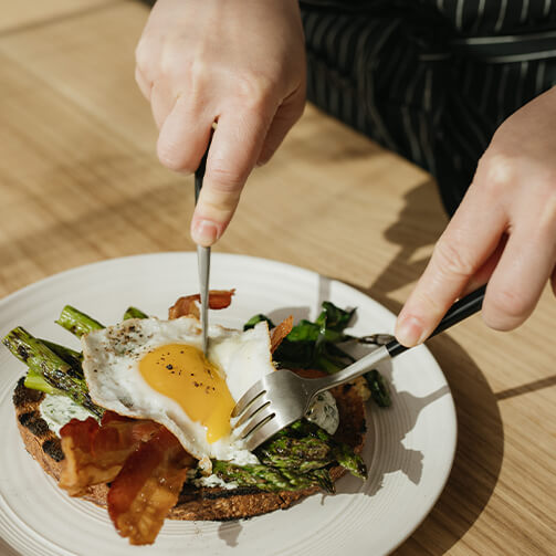 A person slices a soft-boiled egg onto a piece of toast, creating a delicious breakfast scene.