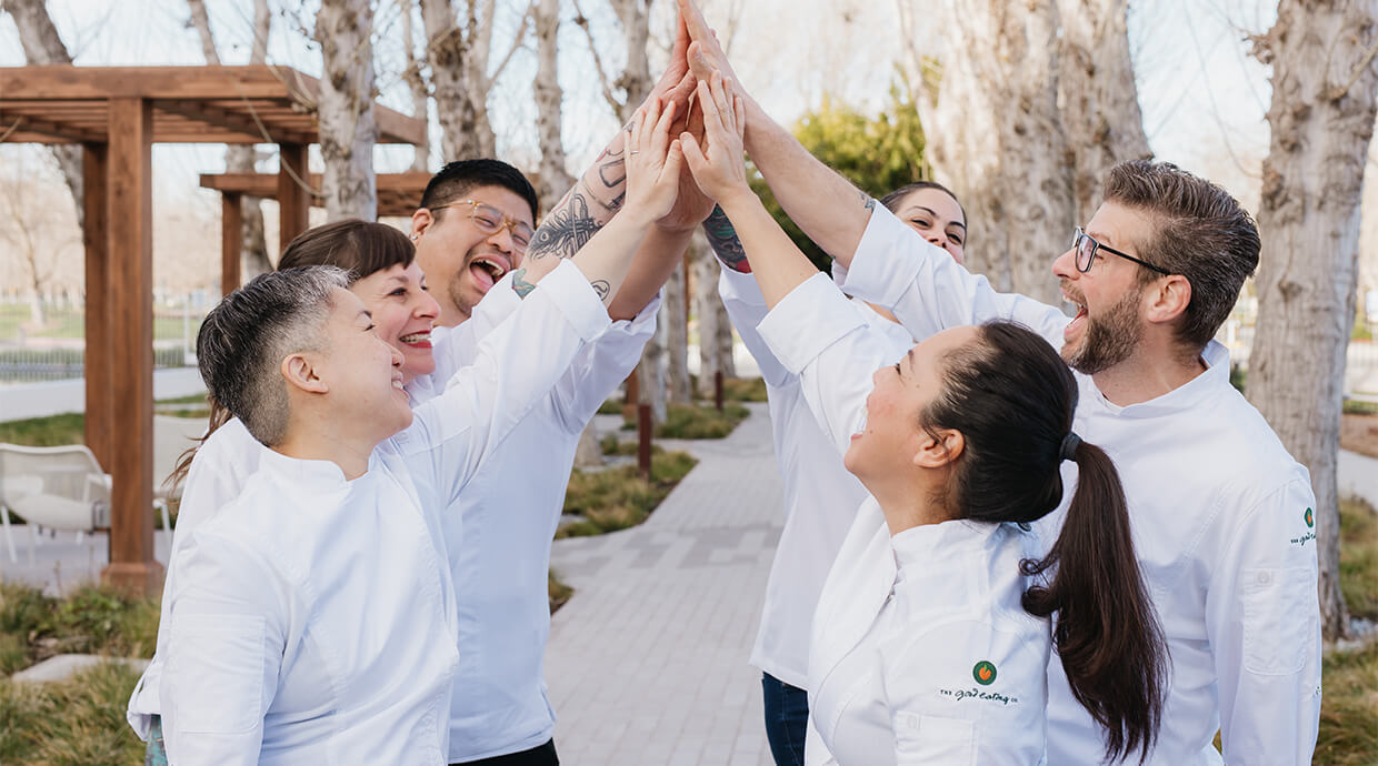A group of chefs celebrating together by giving each other high fives in a lively kitchen setting.