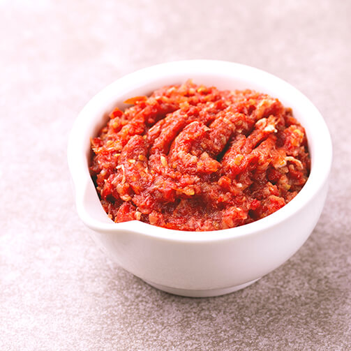 A small white bowl filled with a red, chunky paste, chili paste layers of cumin, coriander, saffron and garlic, harissa adds a smoky heat and a bright, citrusy undertone
