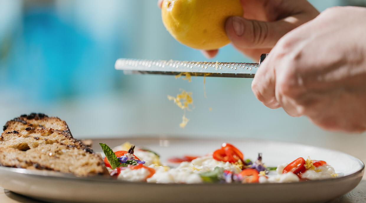 A person slices a lemon on a white plate, showcasing the vibrant yellow fruit and the act of preparation.