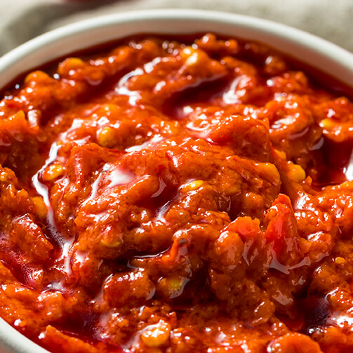 A bowl of chunky red salsa made with tomatoes, peppers, and spices, showcasing a thick, glossy texture