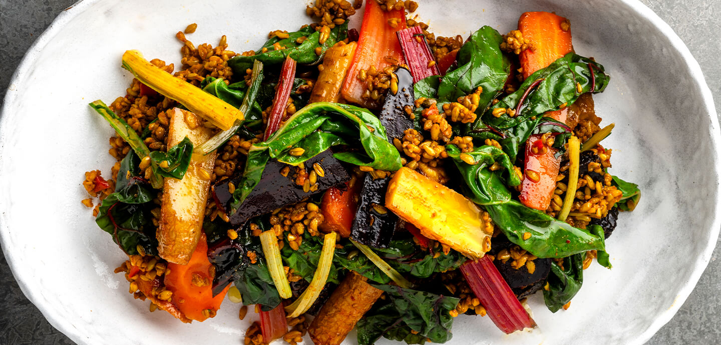 A plate of colorful vegetables including carrots, spinach, and various other fresh greens arranged appetizingly.
