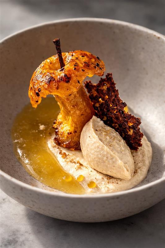 Sobremesa sofisticada com maçã assada e caramelizada, servida com creme de castanha, calda dourada e crocante de cacau, apresentada em bowl claro.