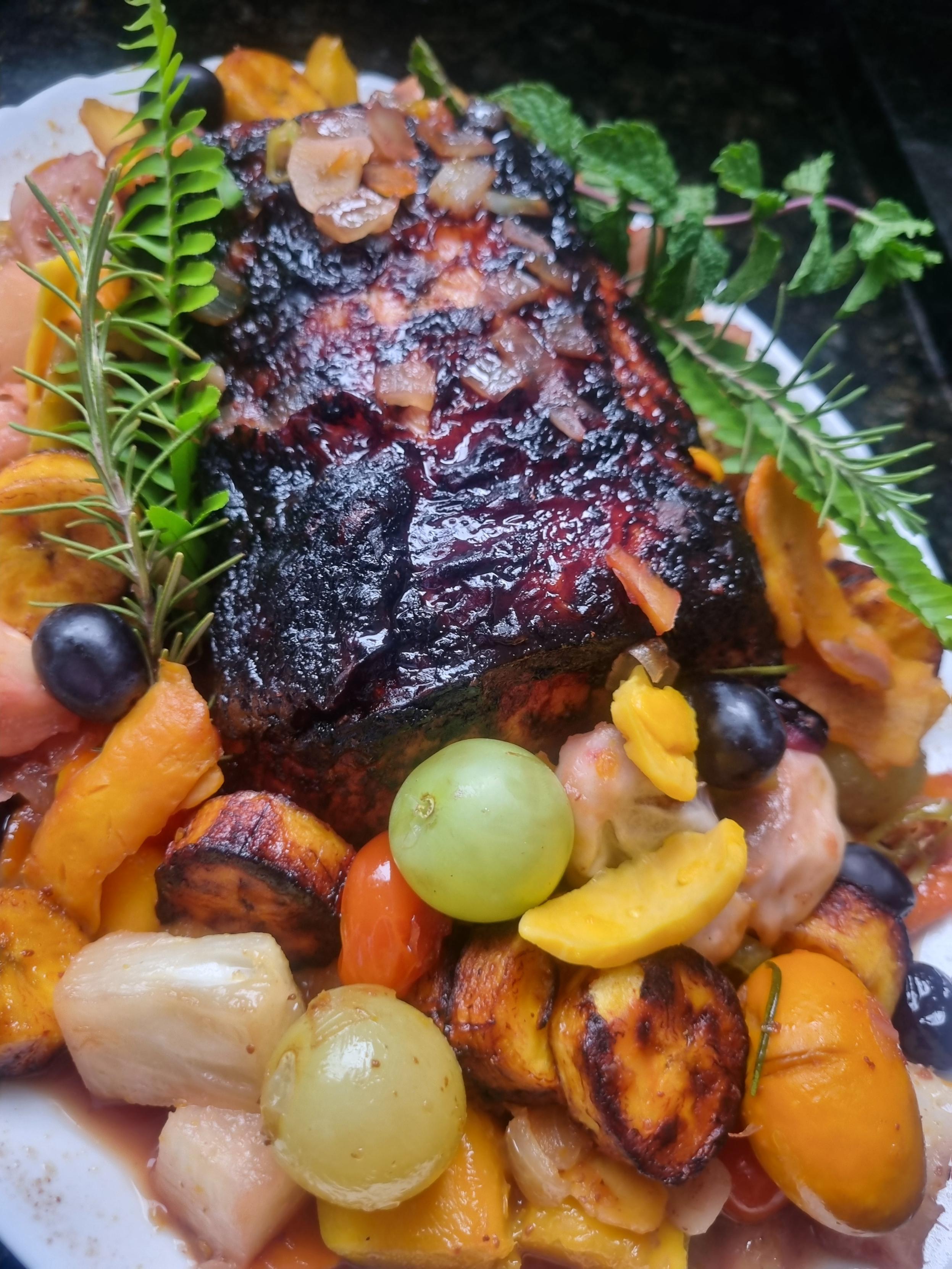 Copa lombo natalino assado e caramelizado, servido em travessa com frutas regionais como uvas, banana-da-terra, buriti, abacaxi e mangaba, decorado com ramos de alecrim e folhas frescas.