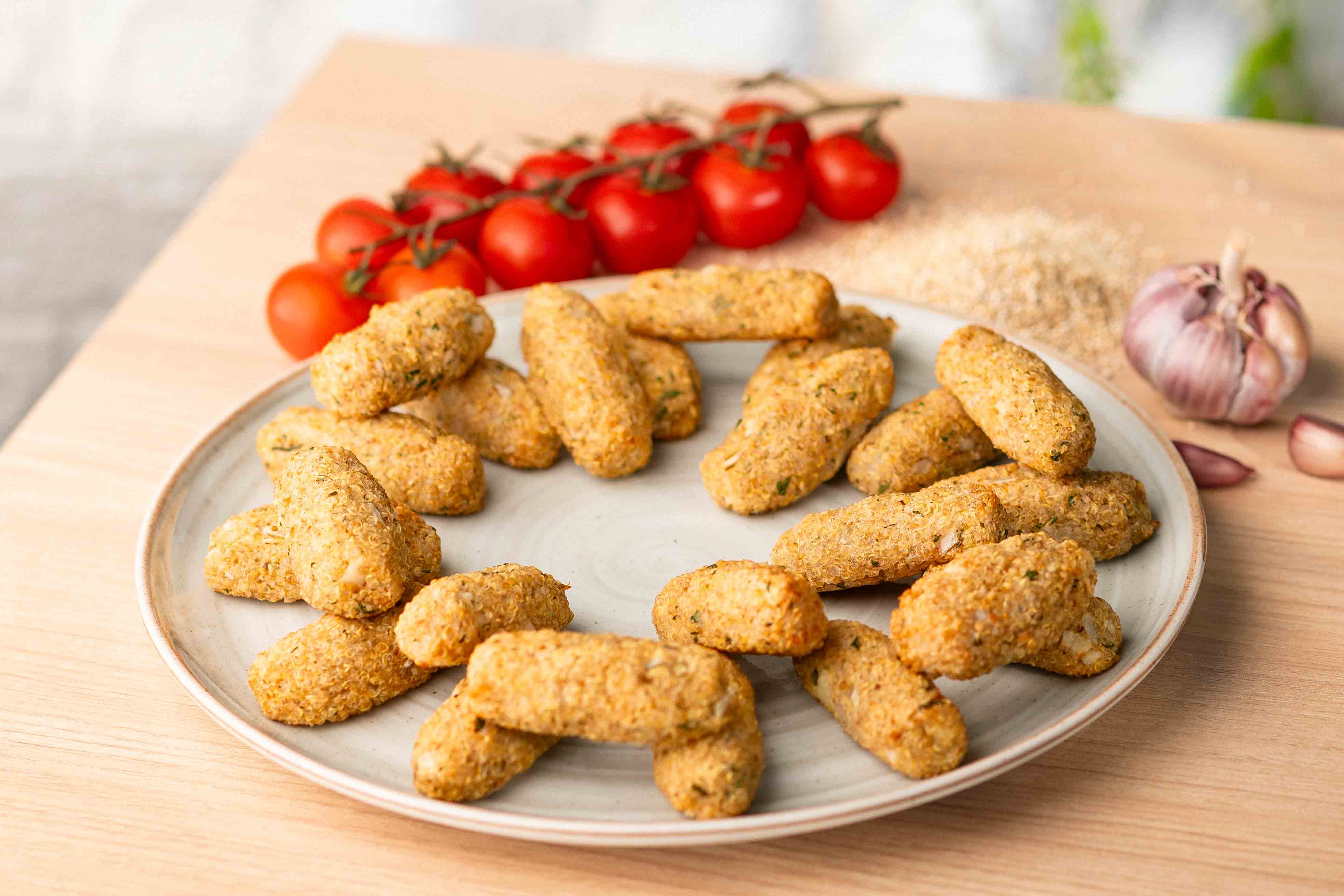Bowl branco com pães de queijo dourados, dispostos sobre mesa de madeira clara, com assadeira vermelha desfocada ao fundo. 