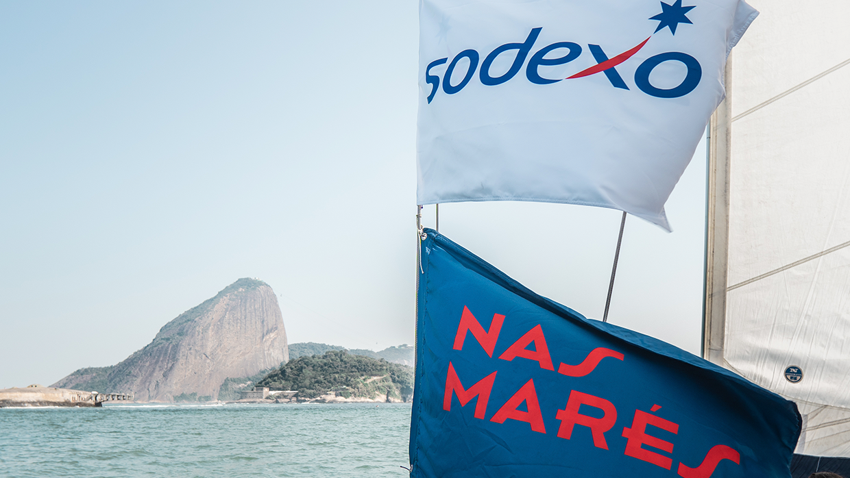 barco em alto-mar com as duas bandeiras, uma azul e a outra branca com os logos da Sodexo e da Nas Marés