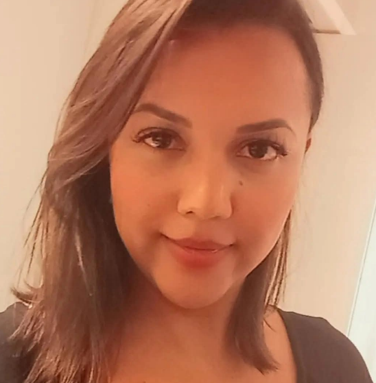 Retrato em close de uma mulher com cabelos castanhos lisos na altura dos ombros, maquiagem leve e expressão suave, olhando diretamente para a câmera, em ambiente interno com fundo claro.