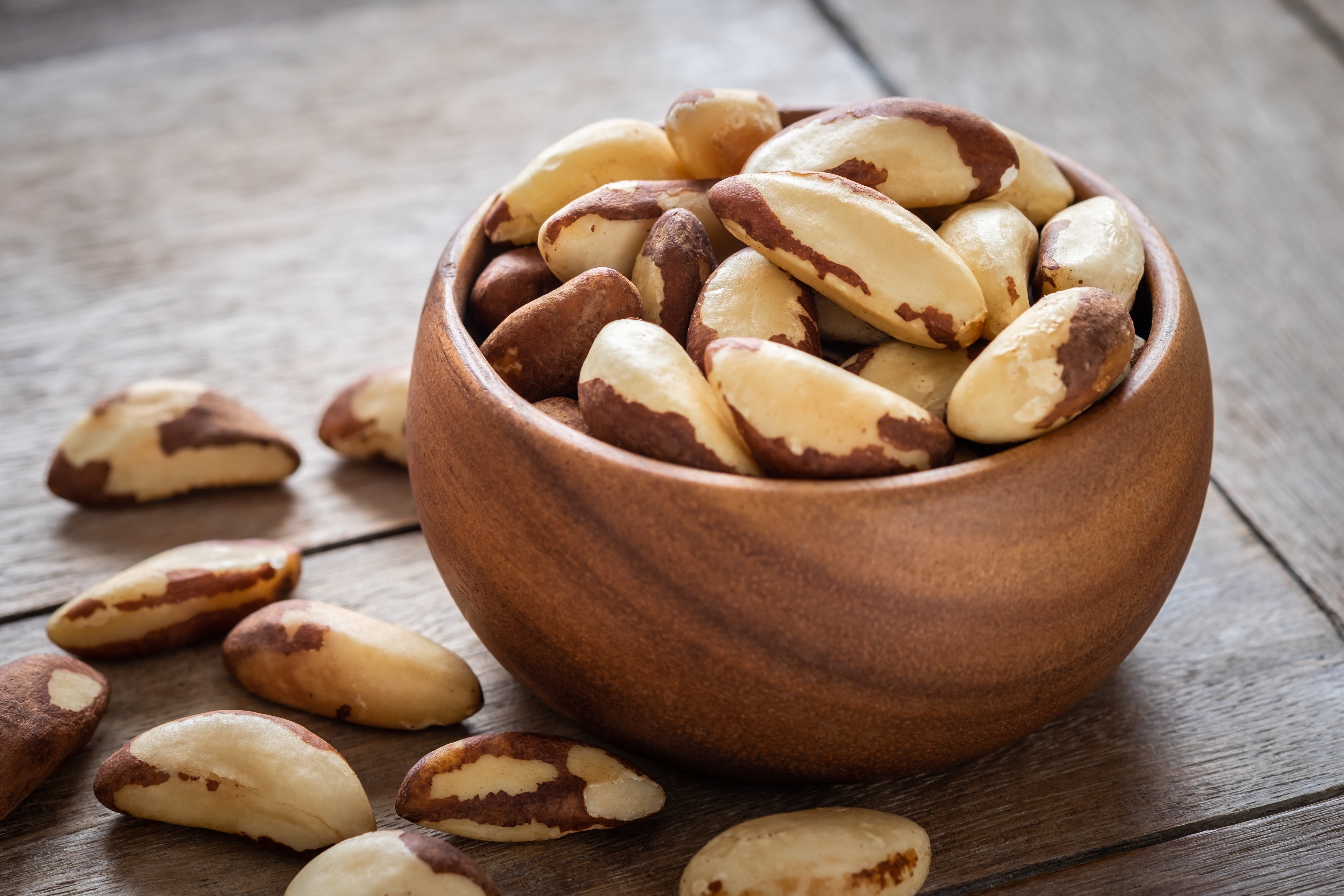 Uma tigela de madeira repleta de castanhas-do-pará, com algumas castanhas descascadas em primeiro plano e outras com casca ao fundo. A imagem destaca a textura e o tom marfim das castanhas, transmitindo a sensação de um alimento nutritivo e saboroso.