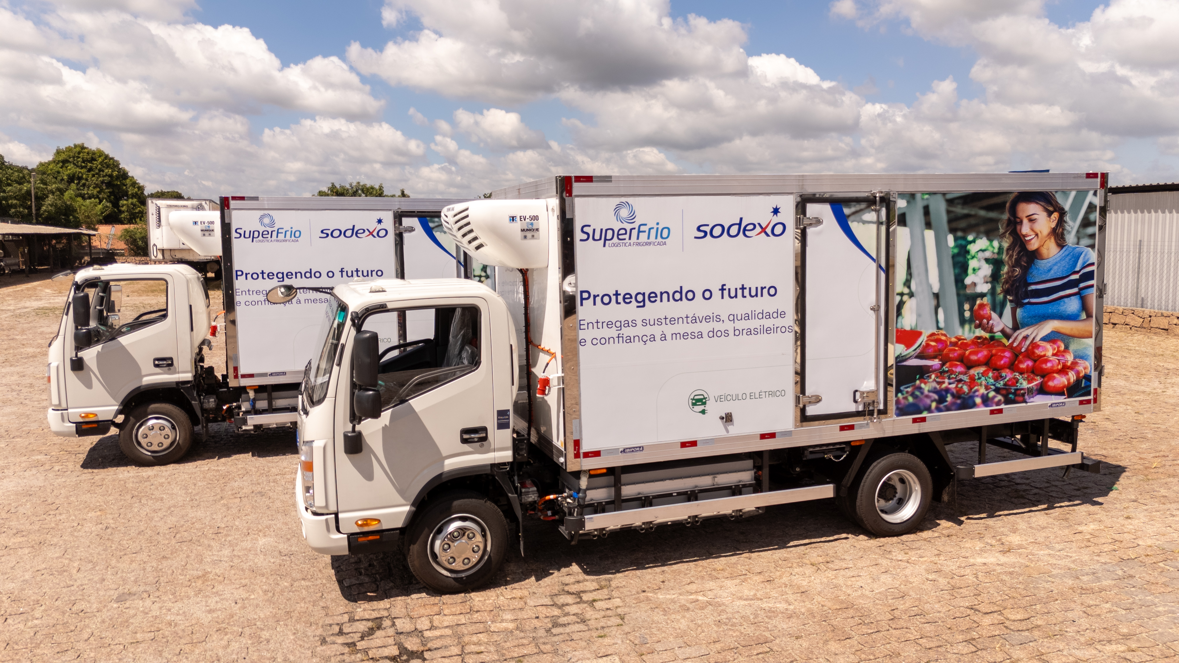 Caminhões elétricos refrigerados da Sodexo e SuperFrio estacionados, com destaque para a mensagem “Protegendo o futuro” nas laterais dos veículos.