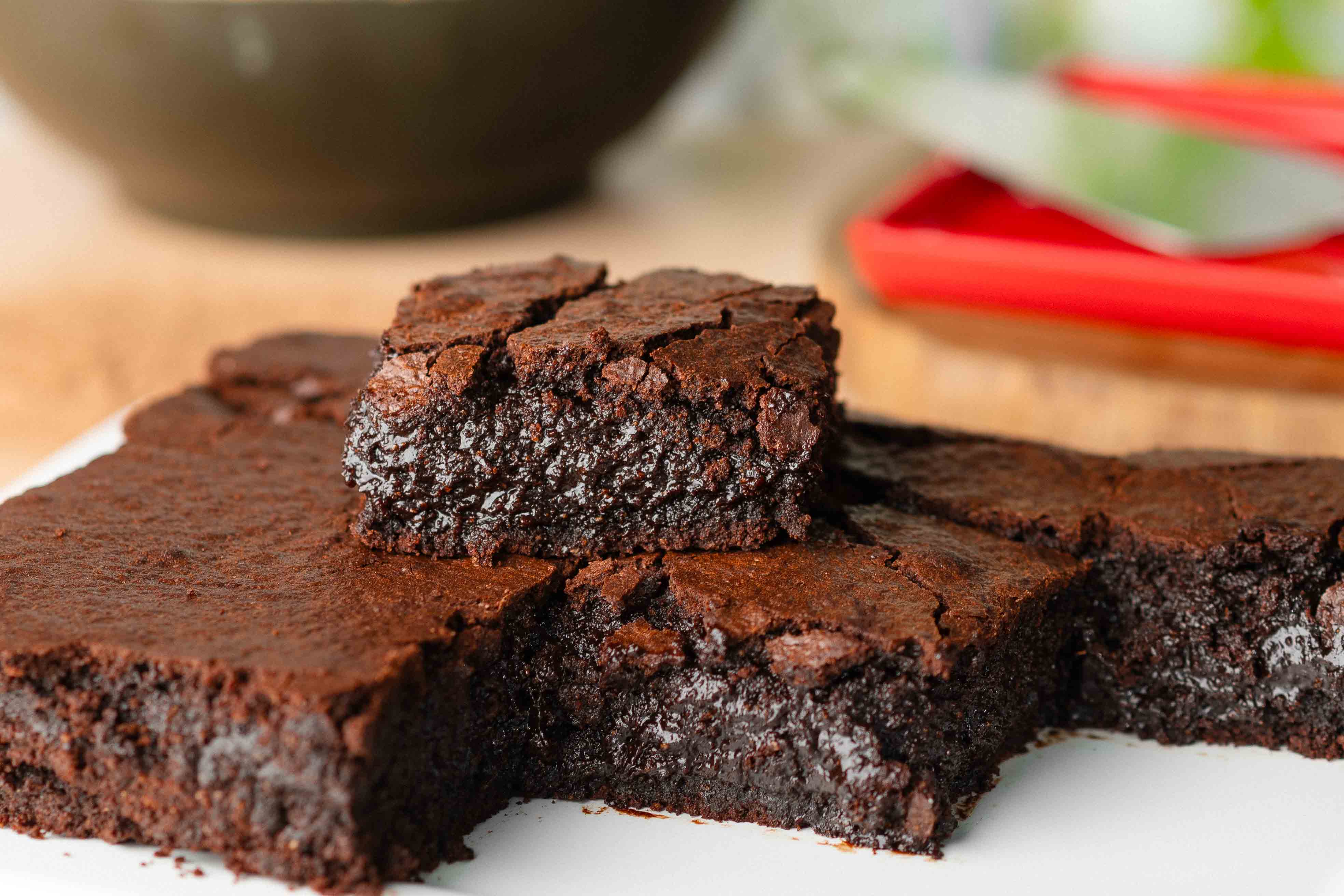 Brownies de chocolate cortados em quadrados, com textura úmida e interior denso. Um pedaço aparece em destaque sobre os demais, servido em um prato branco.