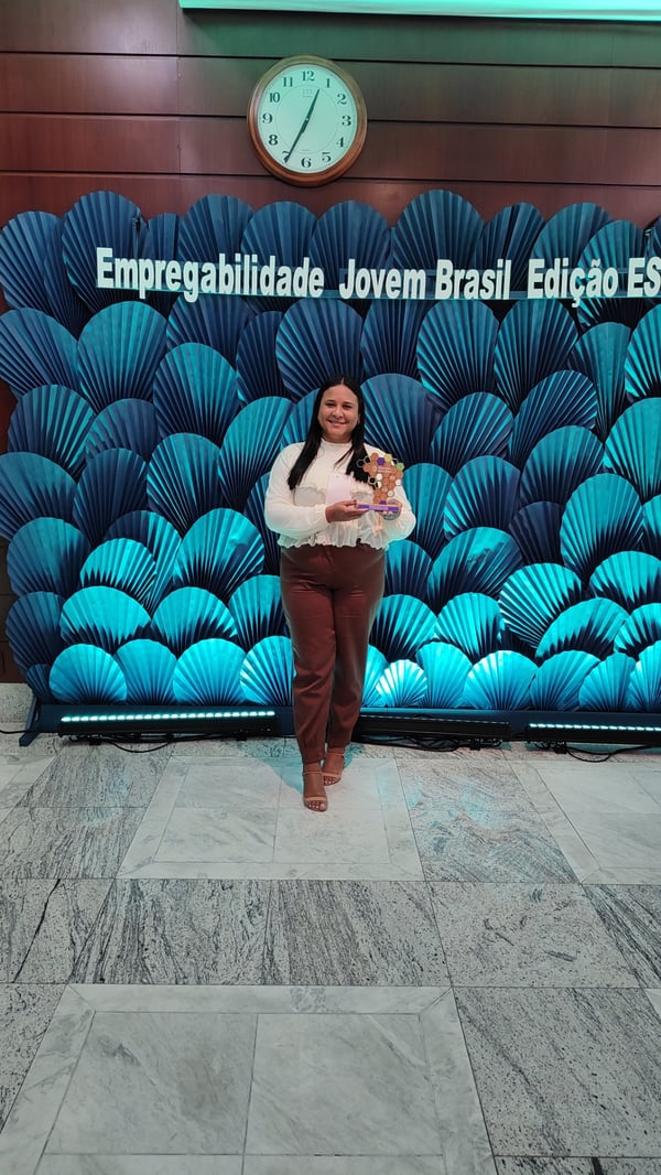 Colaboradora da Sodexo posa com o troféu do Prêmio Empregabilidade Jovem Brasil em frente ao painel de evento.