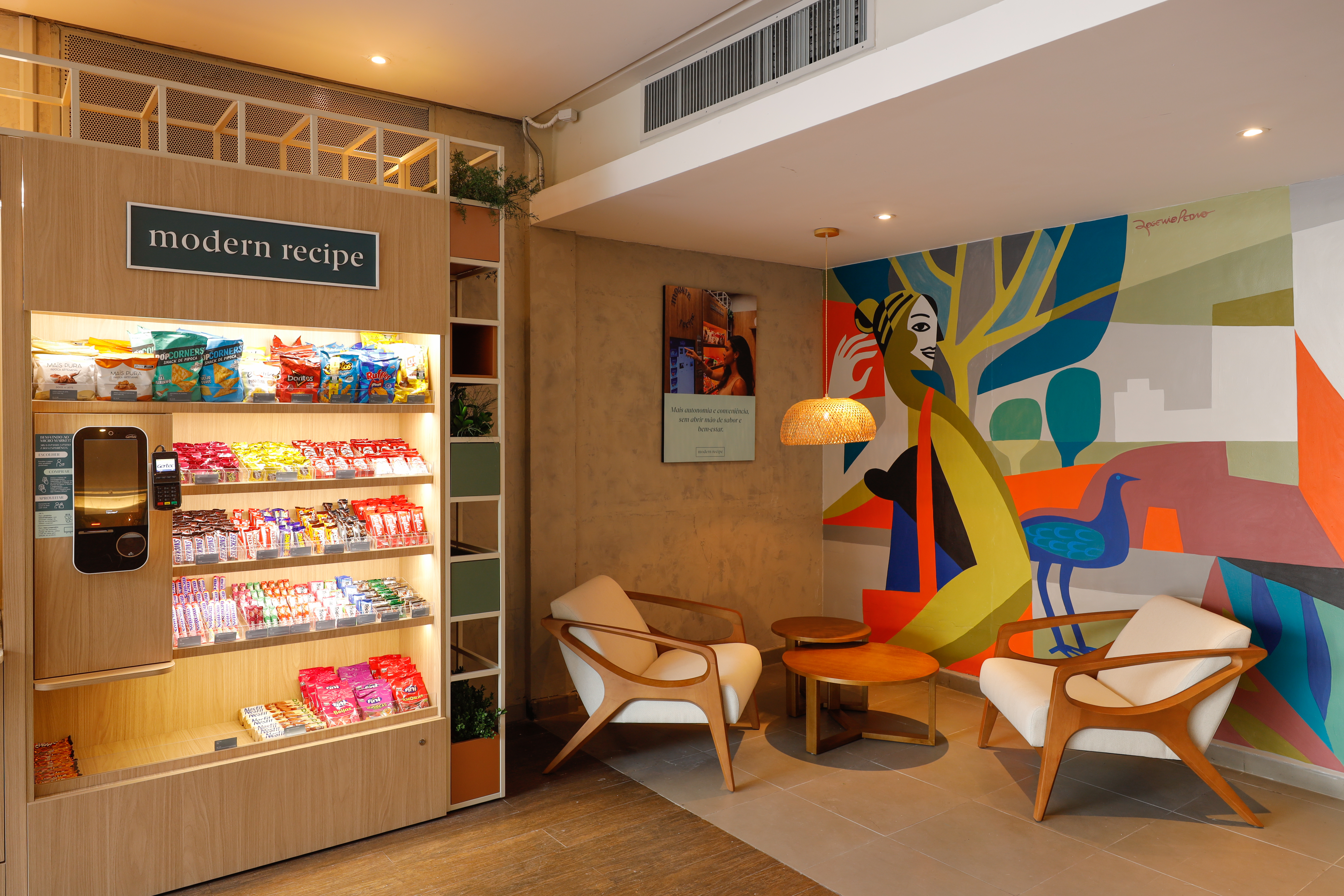 Espaço Modern Recipe com máquina de autosserviço, poltronas, mesas de apoio e mural colorido.