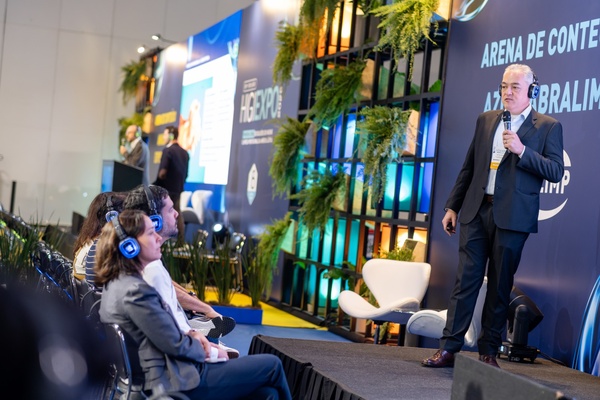Homem de terno apresenta uma palestra no palco da Higiexpo 2026, diante de profissionais que acompanham a apresentação com fones de ouvido.