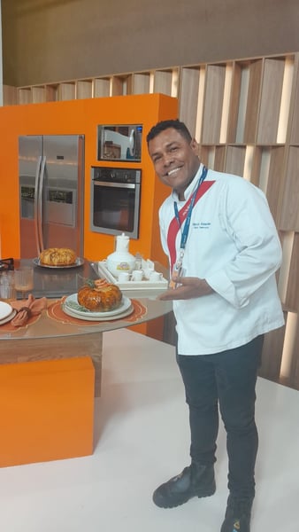 Chef Márcio Anselmo, da Sodexo, posa sorridente segurando o prato de camarão na moranga já finalizado. 