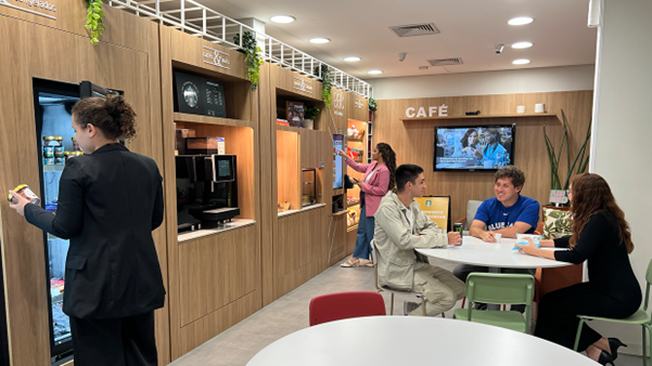 Espaço de compras com pessoas em mesas, onde um refrigerador se destaca, proporcionando um espaço para interação social. 