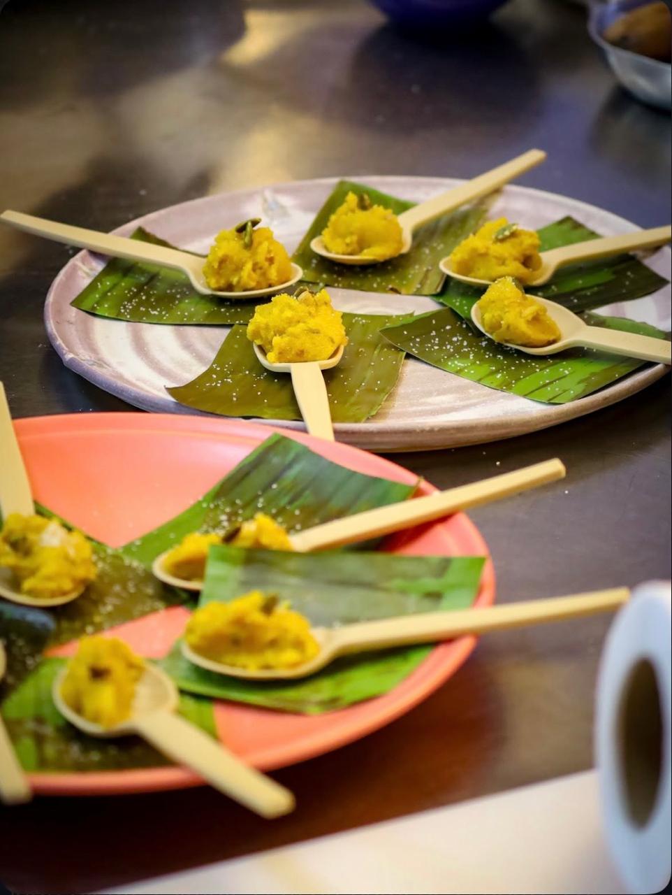Brigadeiros de abóbora servidos em pequenas colheres de madeira sobre folhas verdes, dispostos em pratos coloridos. 